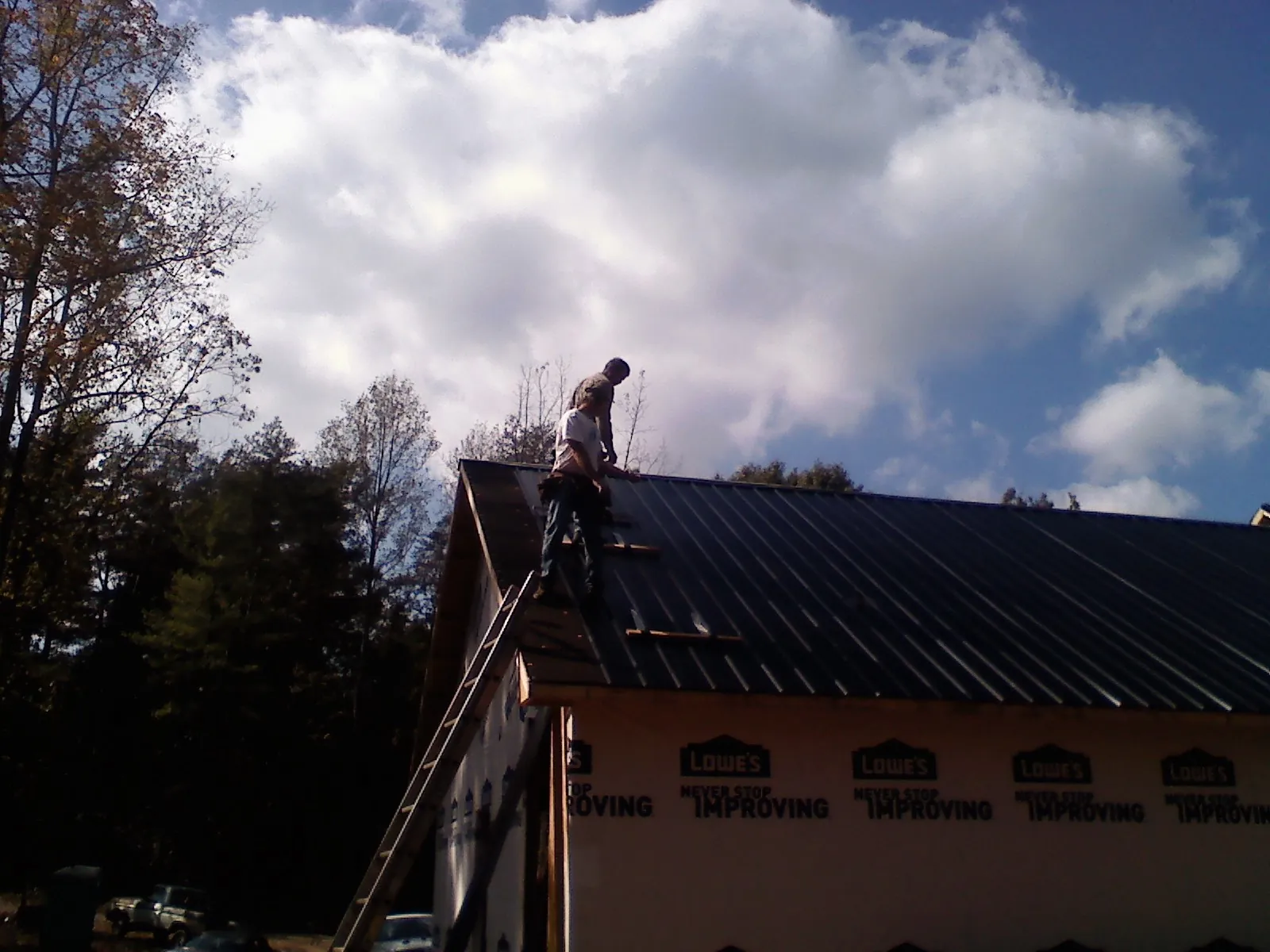 Roofer fastening dark metal panels high against a cloudy sky, from a Roof Inspection job in Palmerton