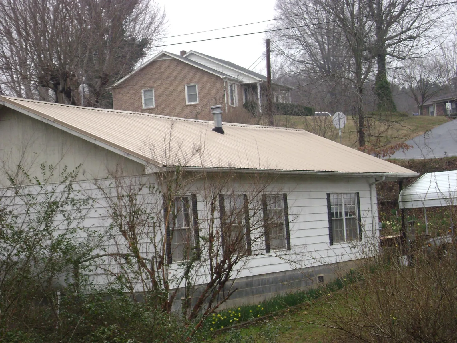 Tan metal roof on a white sided house set into a hillside — Commercial Roofing by Roofing Brothers in Palmerton